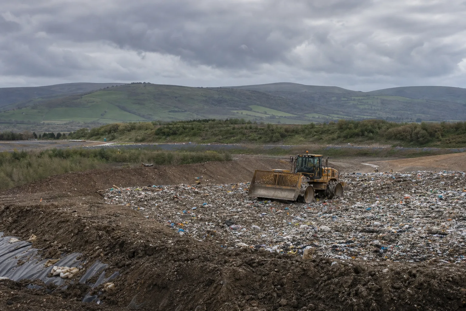 Compaction vehicle working on a modern UK landfill site under overcast sky